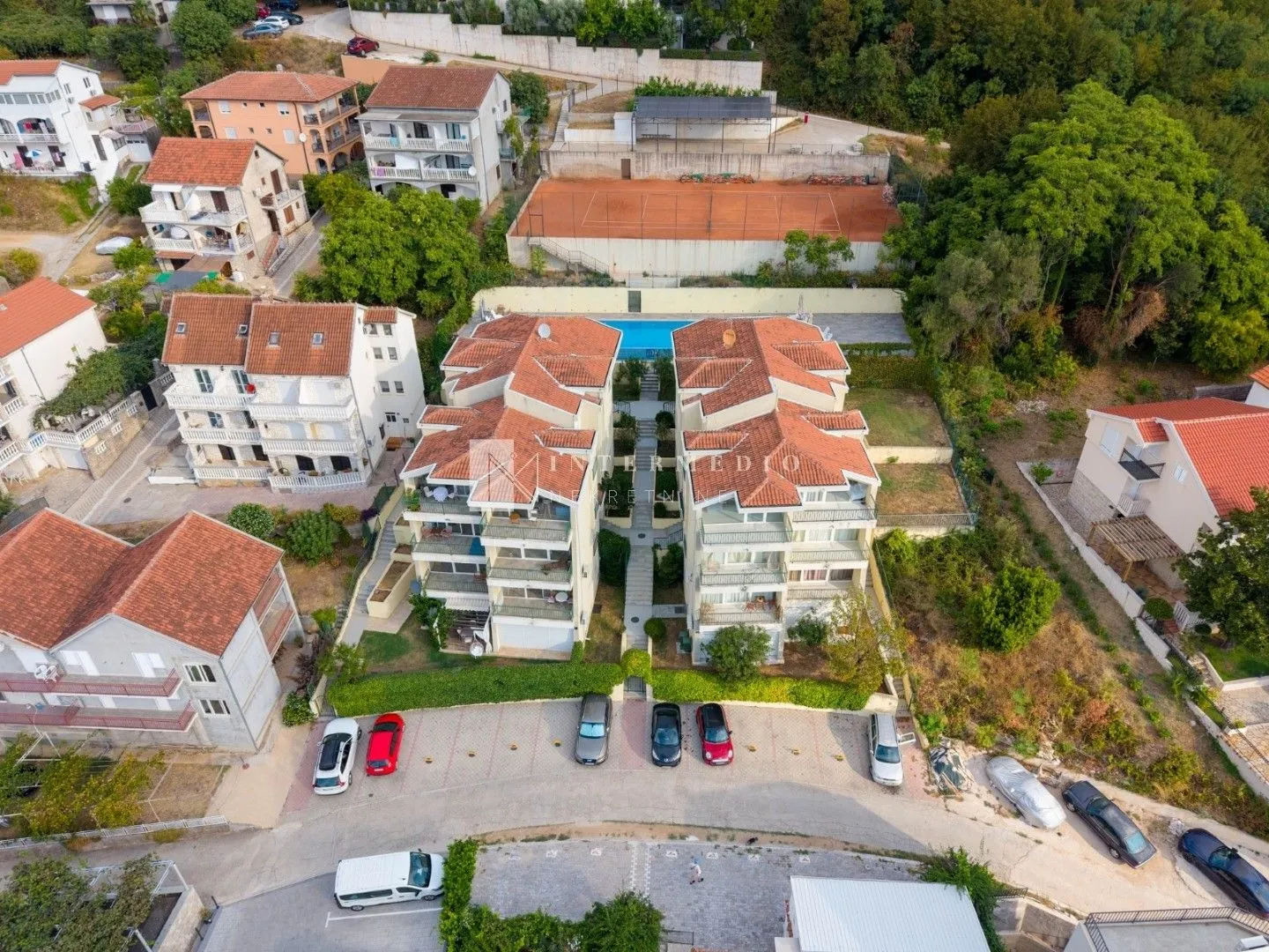 Pogled iz vazduha na stambene zgrade sa bazenom i teniskim terenom.
