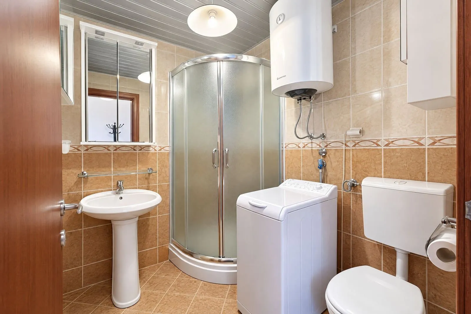 Compactly equipped bathroom with a shower cabin, sink, toilet, and washing machine.
