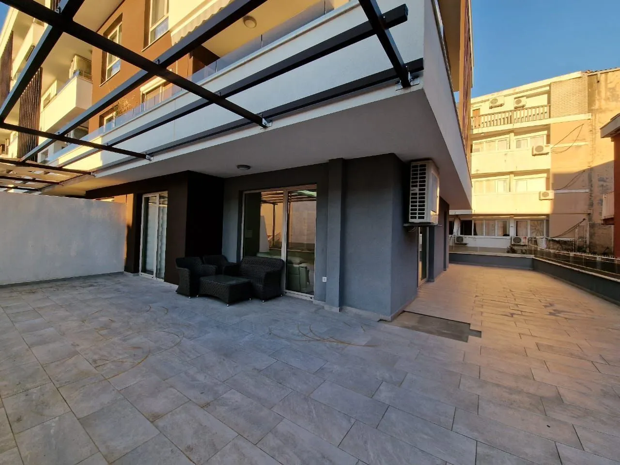 Large tiled terrace with seating furniture on the ground floor of the building.