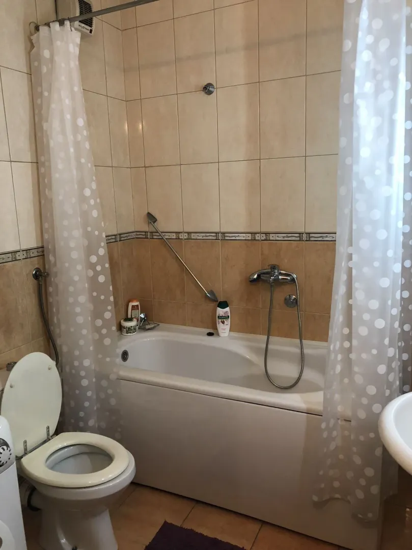 A bathroom with a bathtub, white curtain, and toilet.