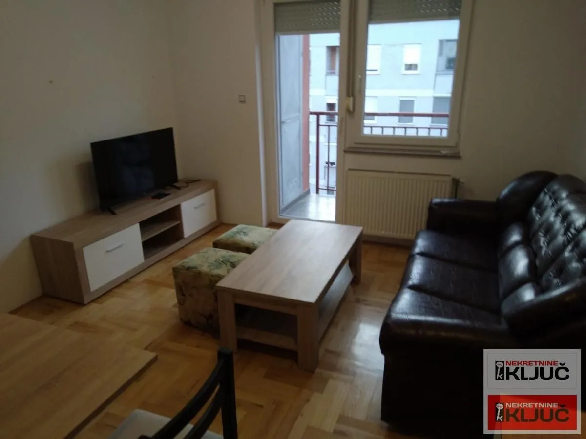 Dnevna soba sa garniturom, televizorom i izlazom na terasu.