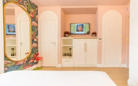 Spavaća soba sa roze zidovima, tapetama sa motivom flamingosa i televizorom. - image 11