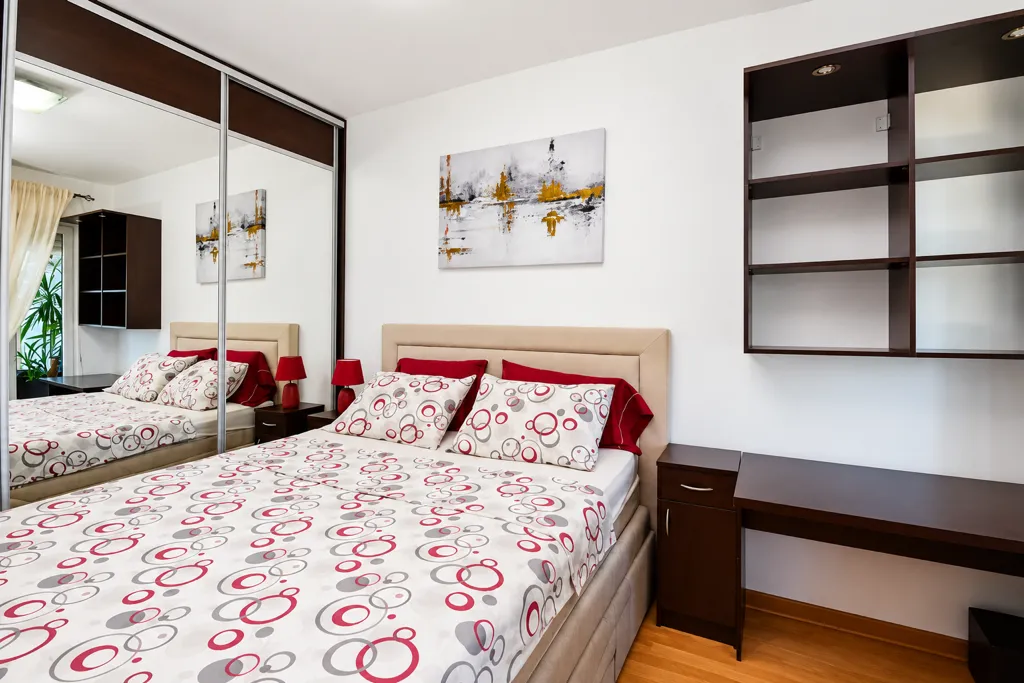 Furnished bedroom with a double bed, mirrored wardrobe, and a desk.
