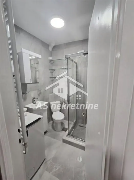 Small bathroom with a shower cabin, sink, toilet, and washing machine.
