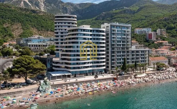 Pogled iz vazduha na moderne višestambene zgrade i plažu u okruženju planina.