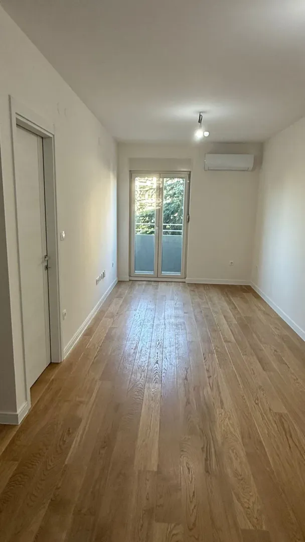 Empty room with wooden flooring, air conditioning unit, and balcony doors.