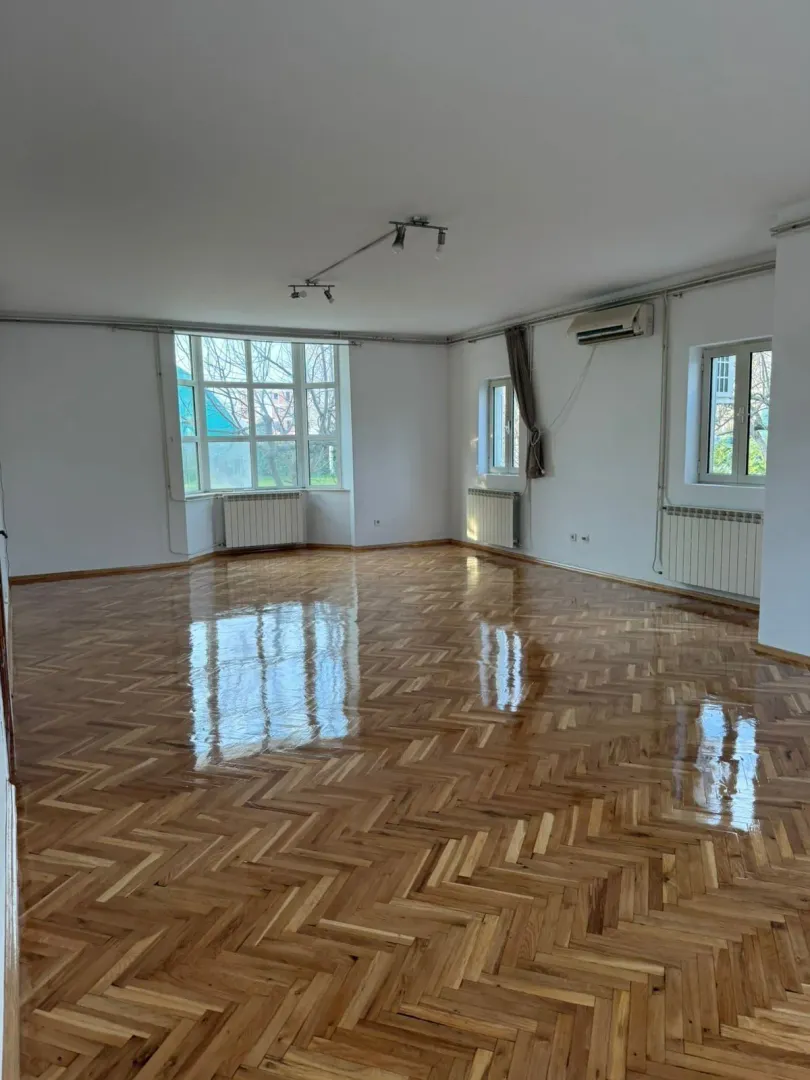 A spacious empty room with glossy parquet flooring and natural light.