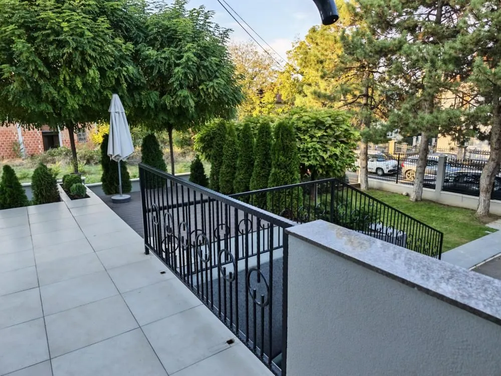 Pogled na popločanu terasu i dvorište puno zelenila.