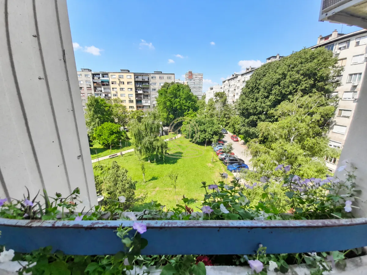 Pogled sa balkona na okolne zgrade i park sa zelenilom.