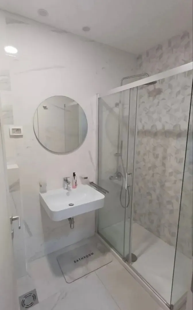 Moderne kupatilo sa umivaonikom, okruglim ogledalom i tuš kabinom.