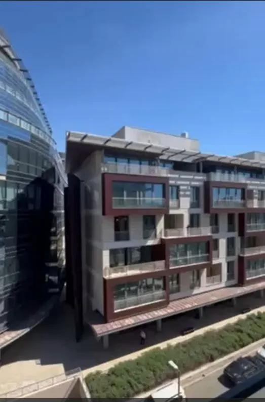 Pogled na modernu stambenu zgradu sa terasama pod plavim nebom.