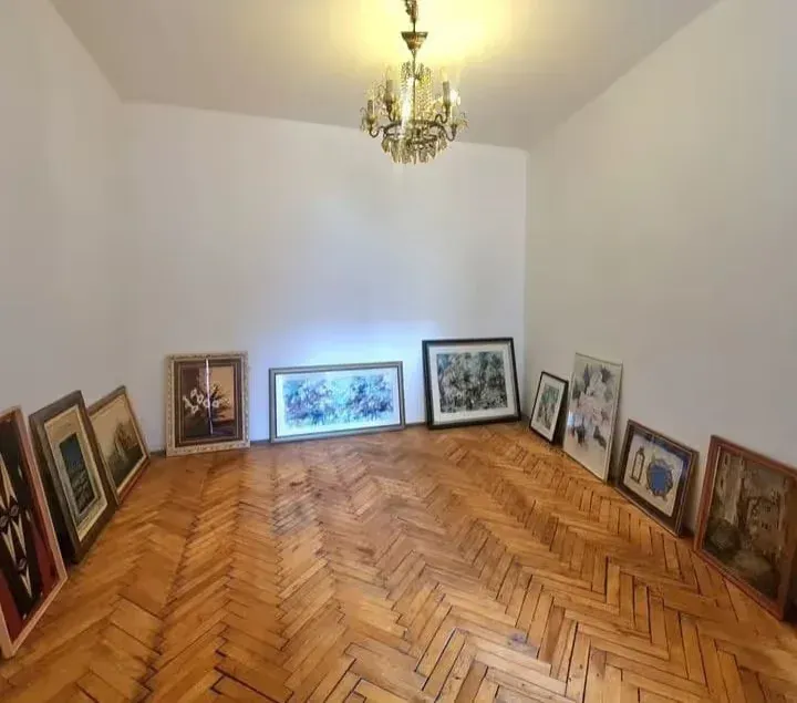 Empty room with wooden parquet flooring and paintings lined up along the walls.