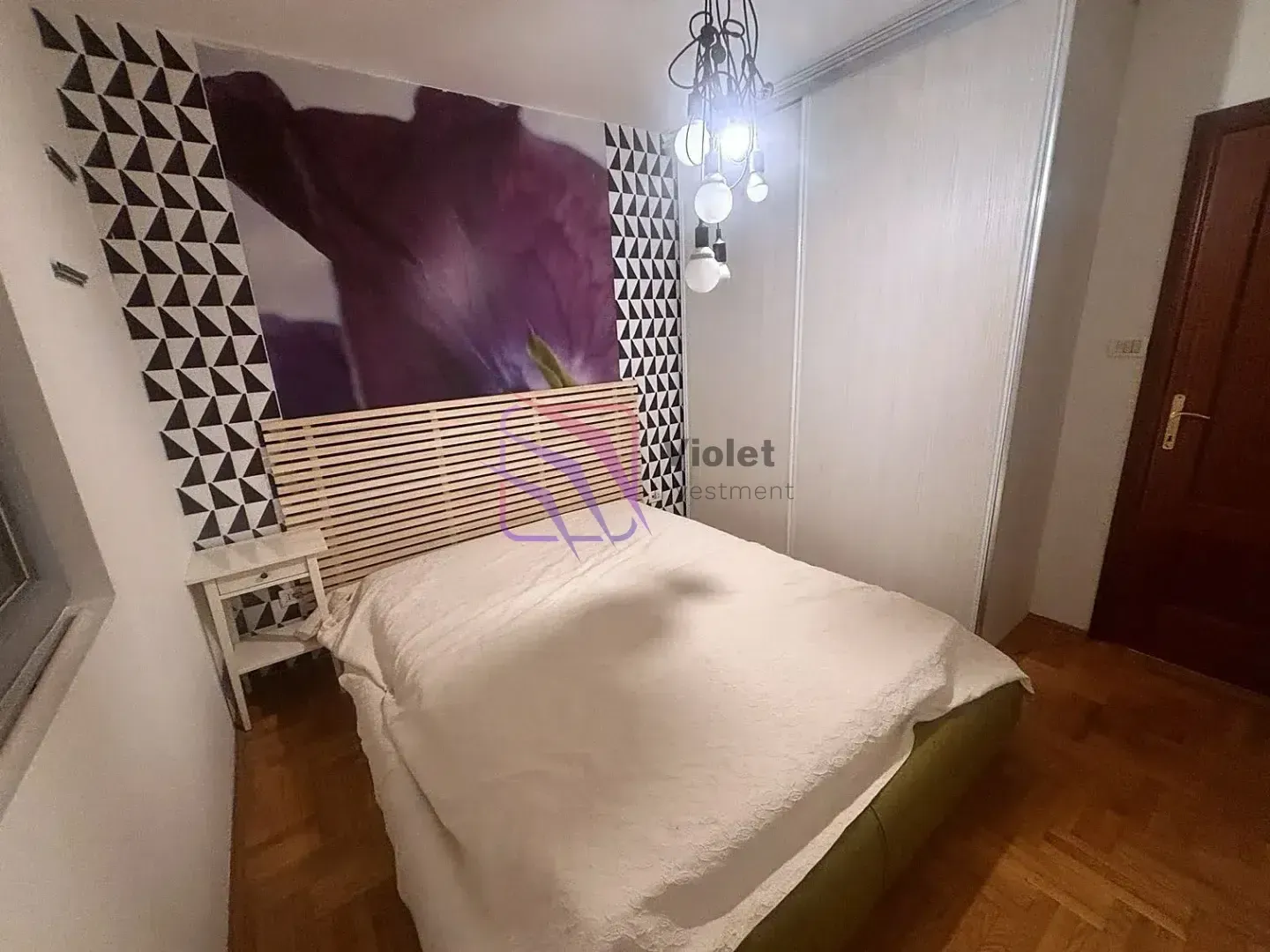 Namještena spavaća soba sa bračnim krevetom, uzglavljem i ugradnim ormarom.