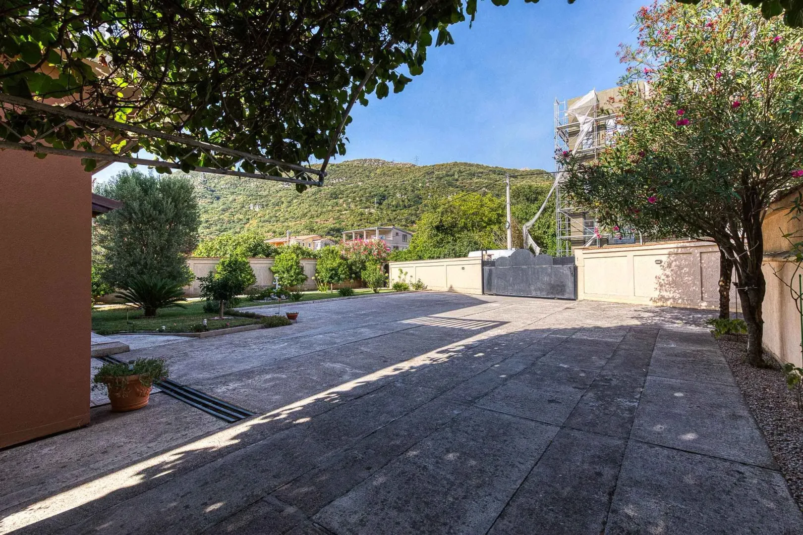 Prostrano popločano dvorište sa zelenilom i pogledom na brda.