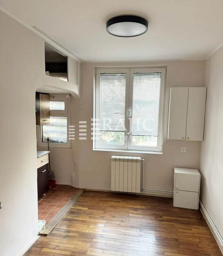 Empty room with wooden flooring, a window, and a passage to the kitchen.