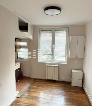 Empty room with wooden flooring, a window, and a passage to the kitchen. - image 2