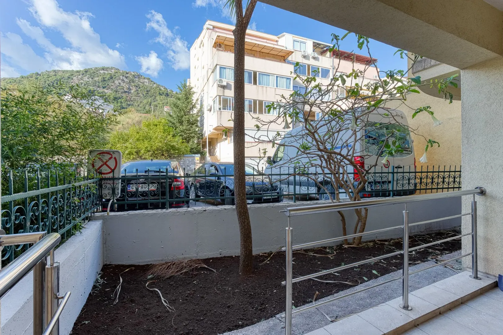 View from the terrace facing the building, yard, and parked vehicles.