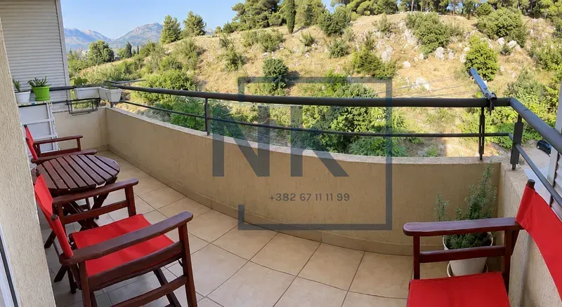 Namješten balkon sa drvenim stolom i crvenim stolicama i pogledom na prirodu.