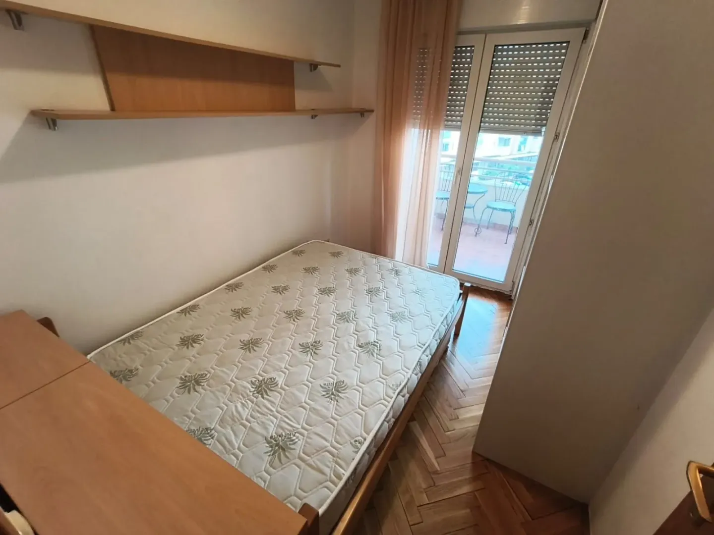Manja spavaća soba sa krevetom i izlazom na terasu.