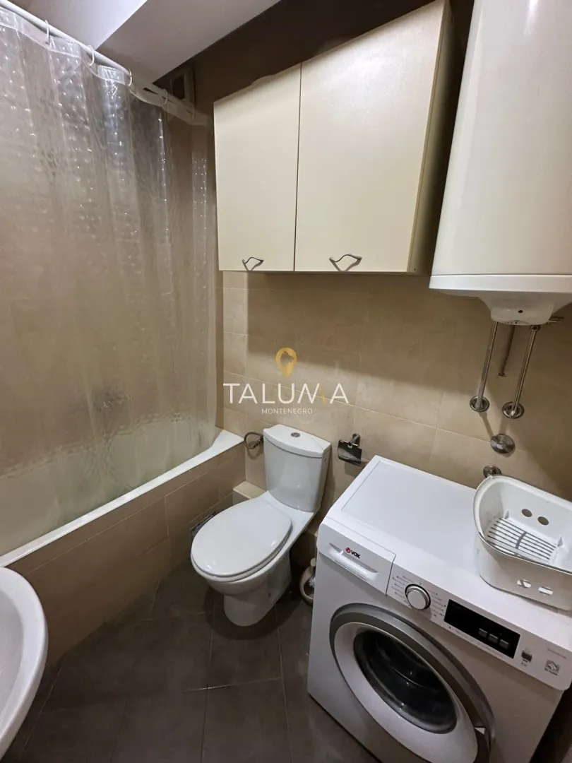 Smaller bathroom equipped with a bathtub, toilet, cabinet, and washing machine.