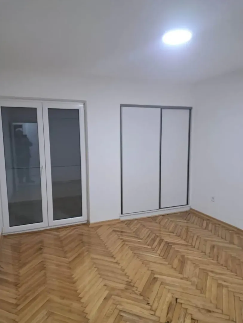 Prazna soba sa parketom, ugradnim plakarom i balkonskim vratima.