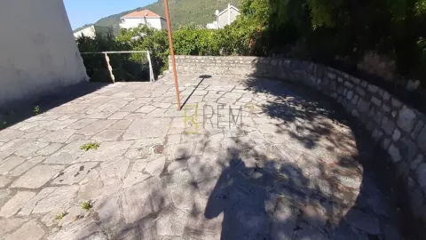 Popločano dvorište sa kamenim zidom i zelenilom u pozadini. - image 19