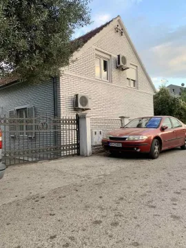 House with white brick facade, gate, and a parked car. - image 4