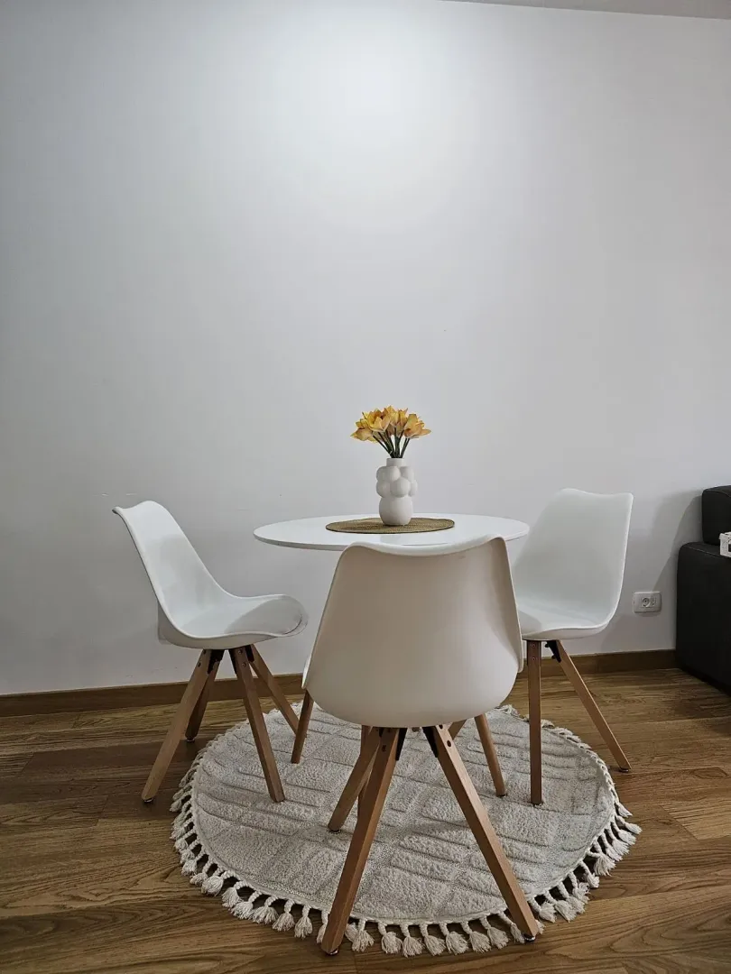 A small round dining table with three white chairs on a decorative rug.