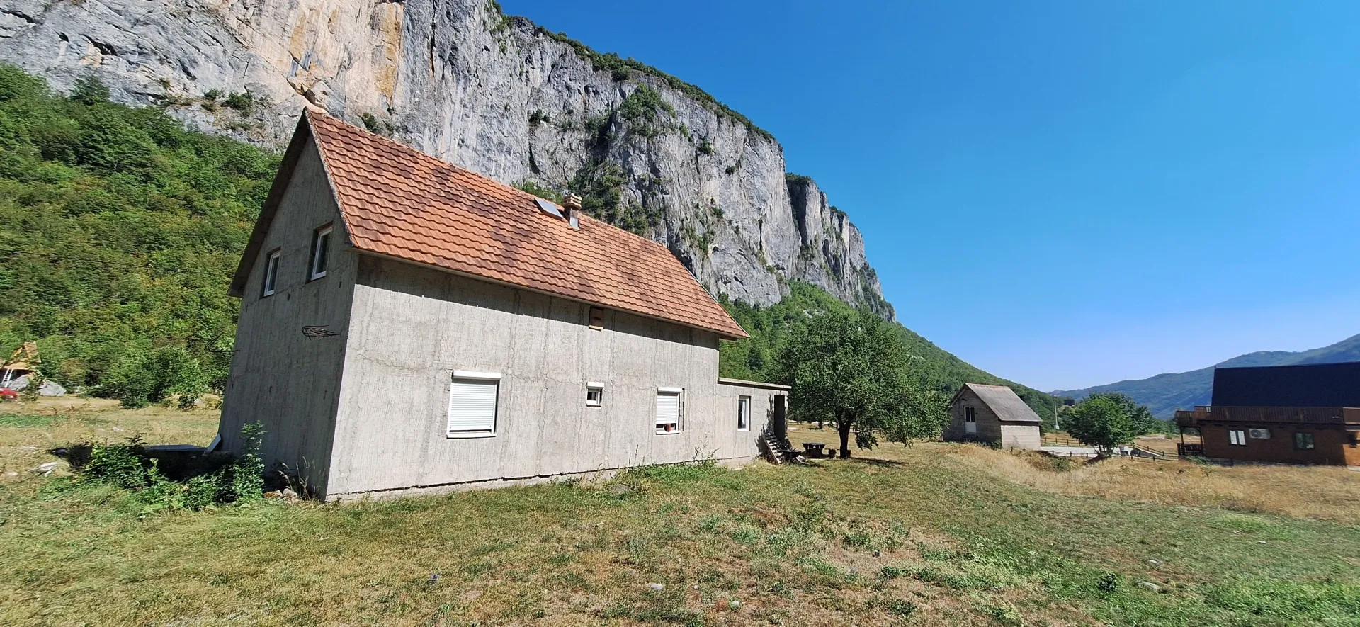 Pogled na kuću sa krovom od crijepa u prirodi pod stijenom.