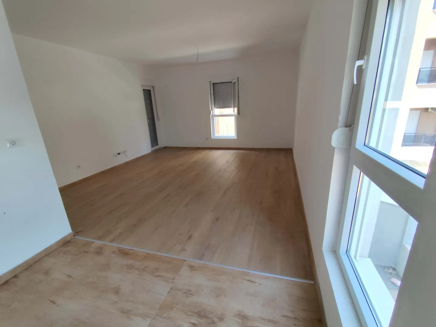 Empty room with white walls, wooden flooring, and windows.