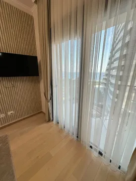 Living room with wooden flooring, a wall-mounted TV, and large balcony doors with curtains. - image 5