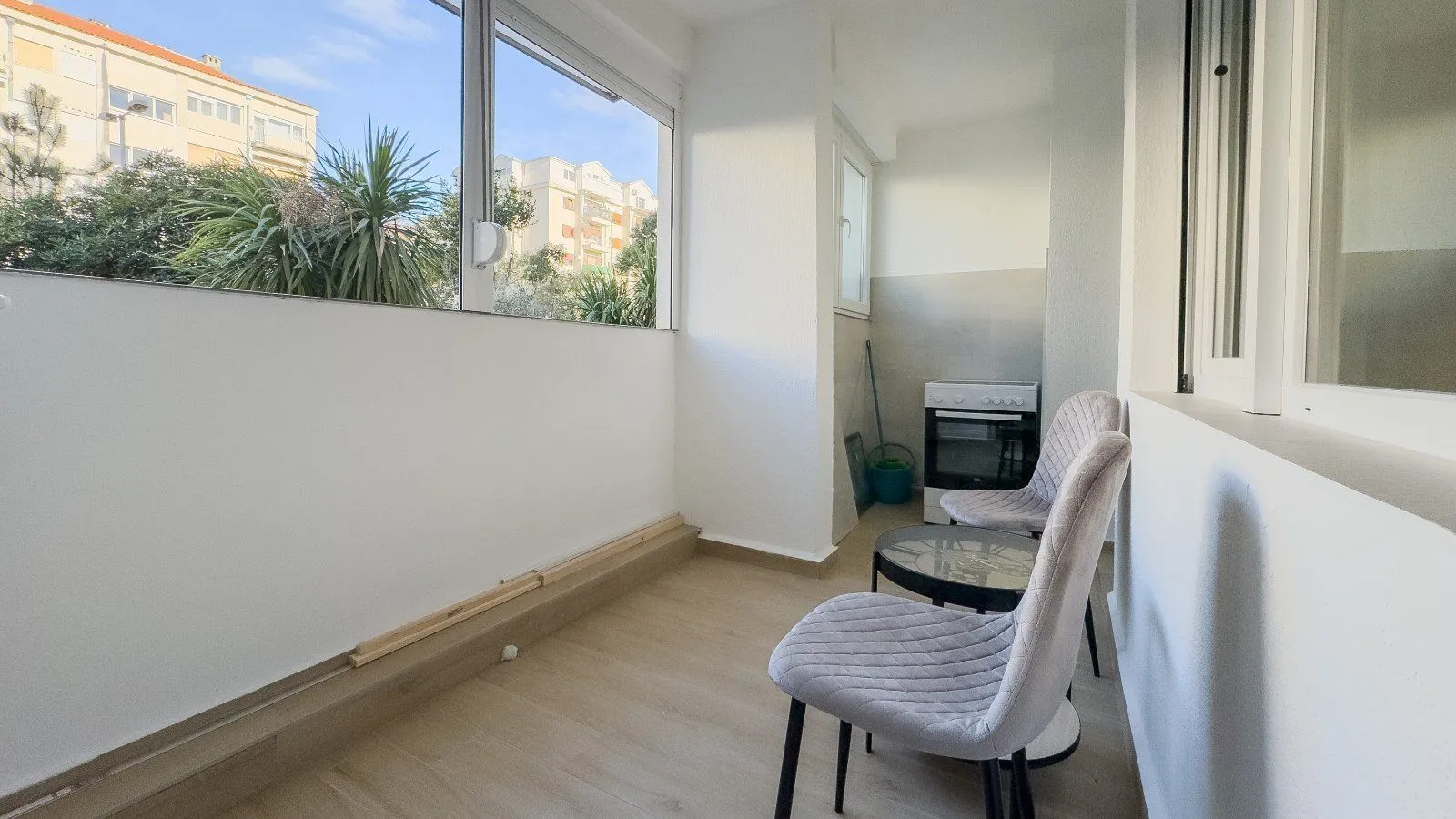 Zastakljeni balkon sa dvije stolice, stočićem i pogledom na naselje.