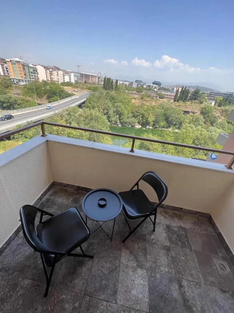 Balkon sa dvije crne stolice i stolićem, sa pogledom na rijeku i grad.