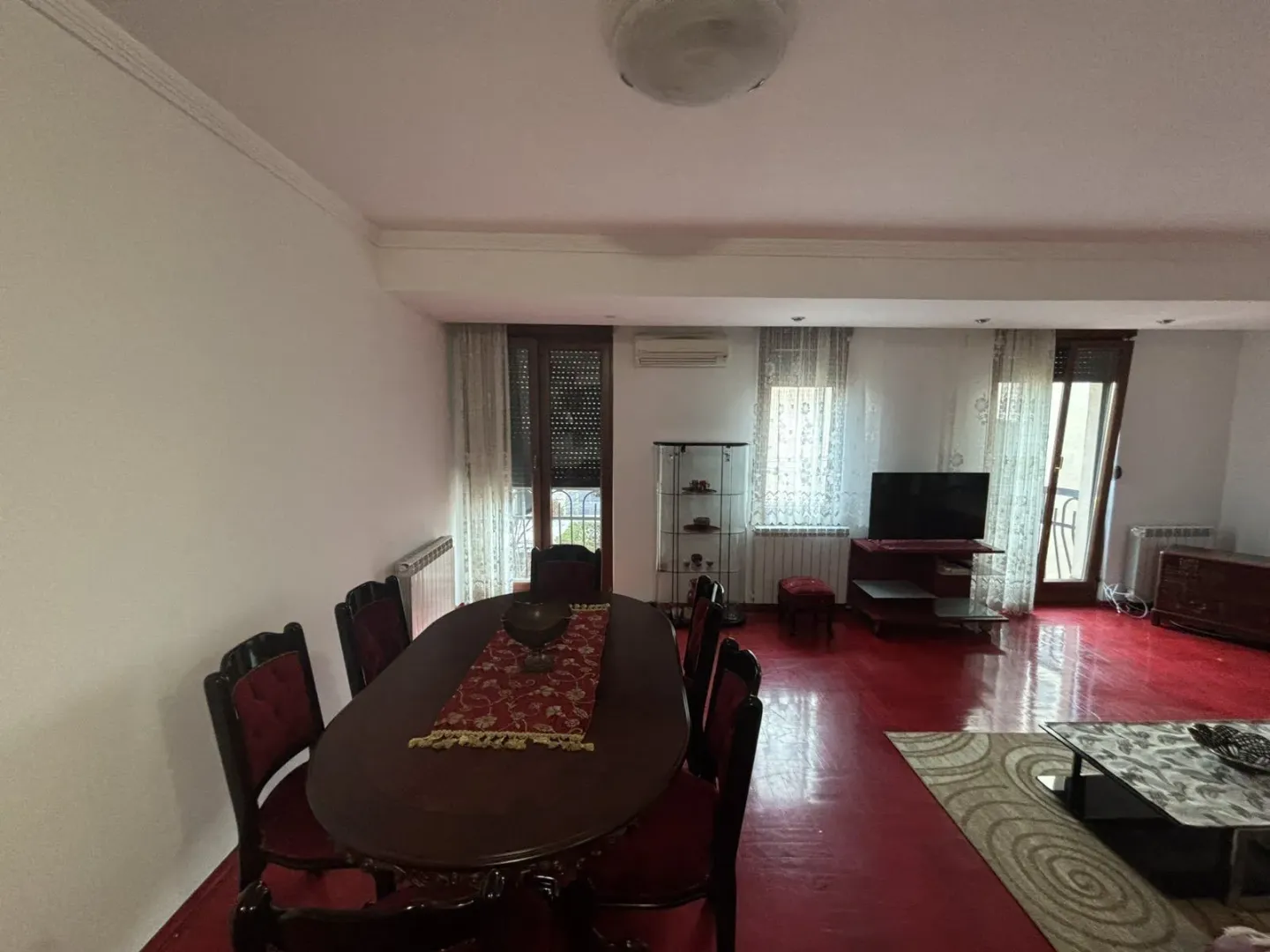Spacious living room with a dining table and red flooring.