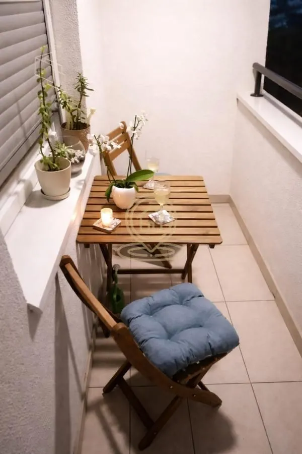 Manji namešteni balkon sa drvenim stolom i stolicama.