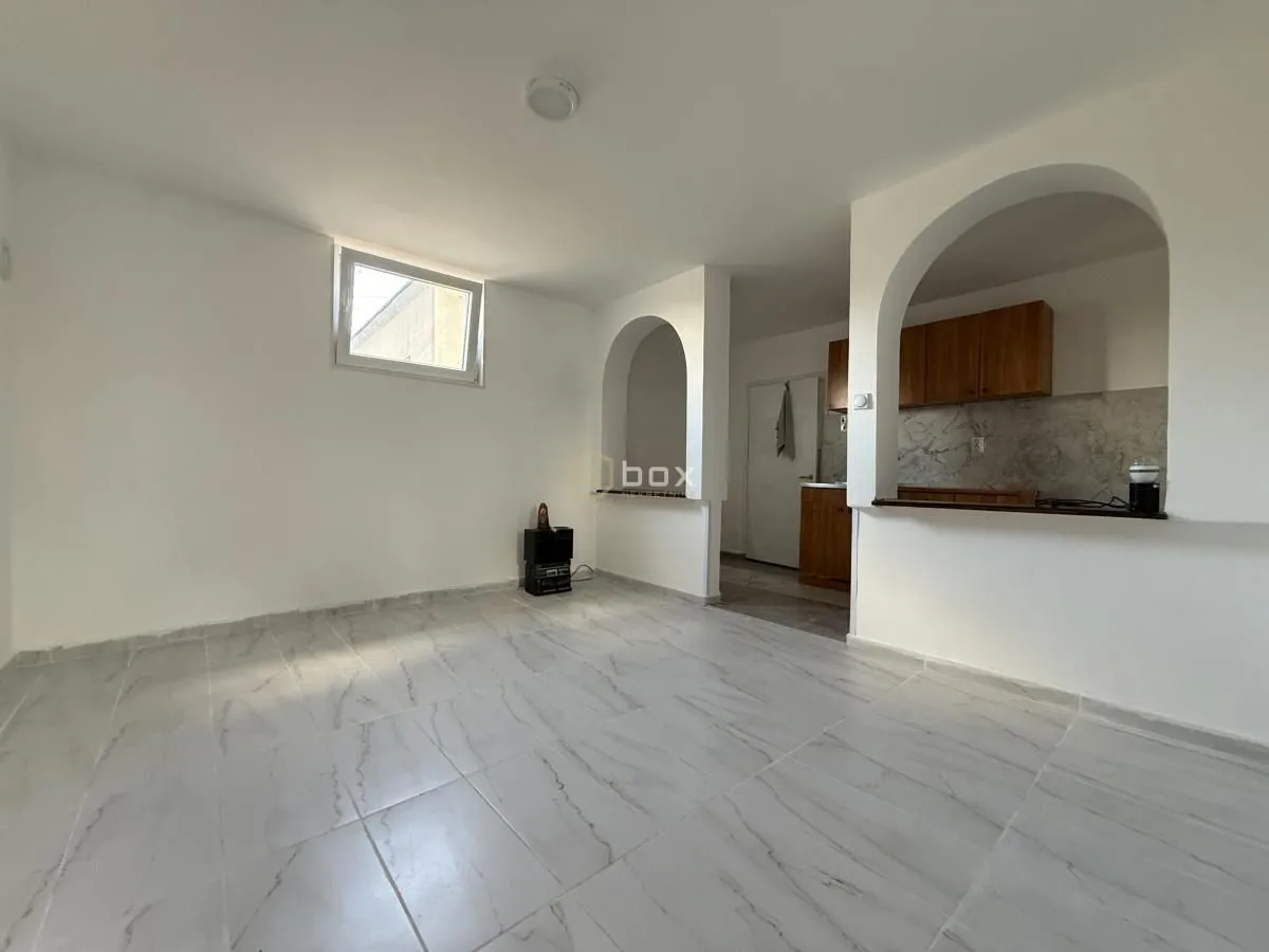 Empty living room with tiled flooring and an arched pass-through to the kitchen.