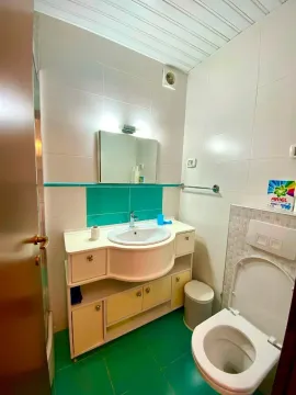 Kupatilo sa bijelim i zelenim pločicama i umivaonikom sa ormarićem. - image 4