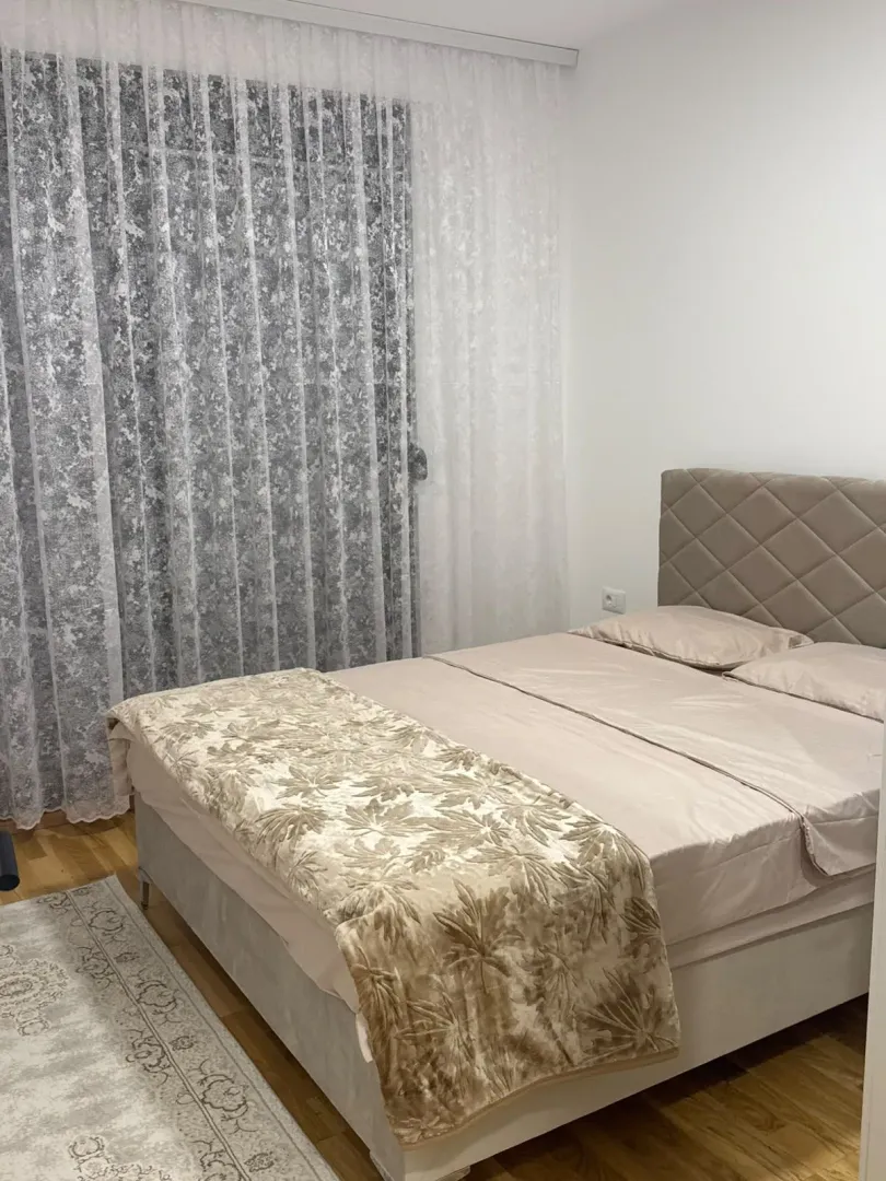 A furnished bedroom with a double bed and a large window with curtains.
