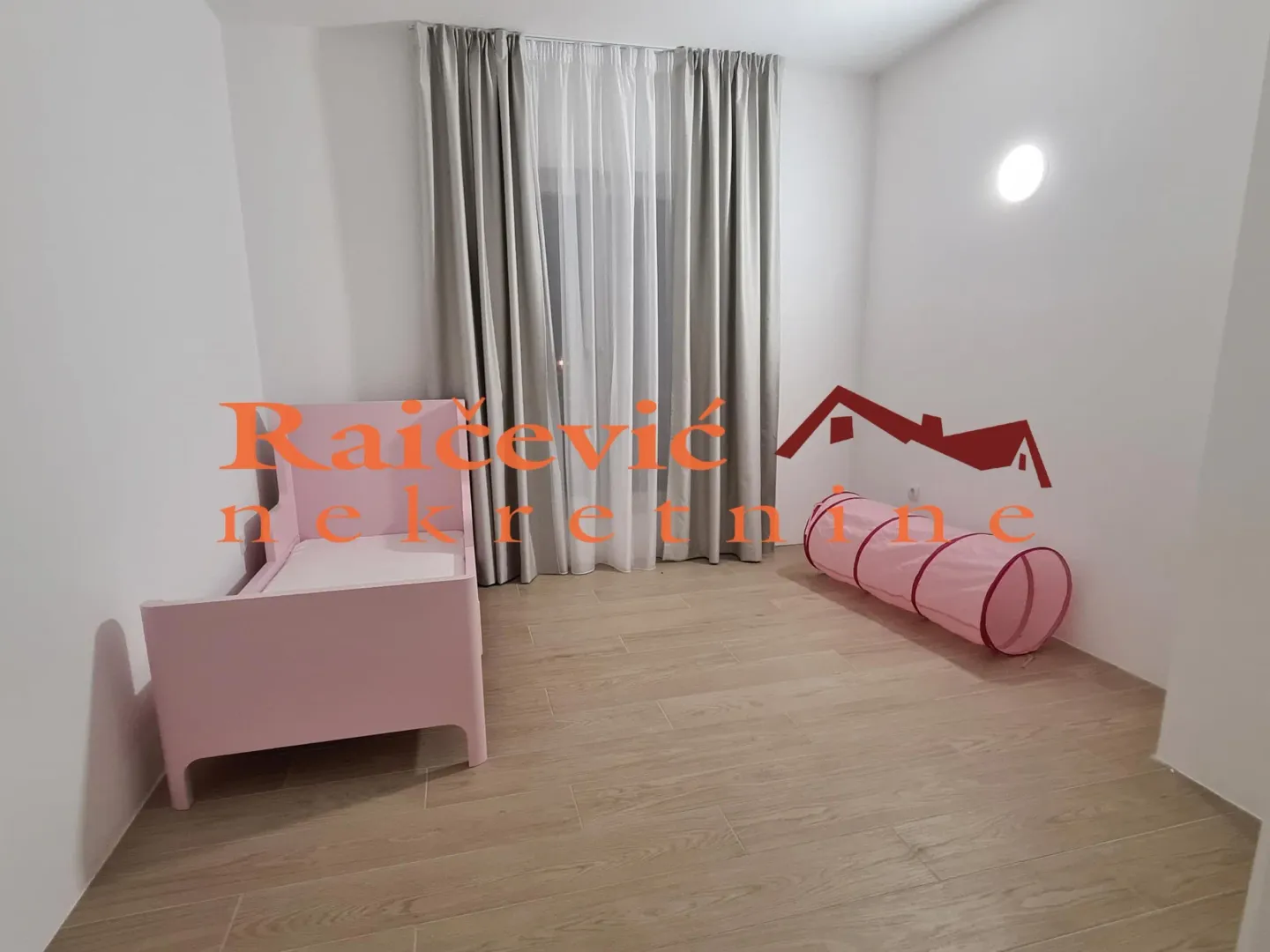 Dečja soba sa roze krevetom, zavesama i igračkama.