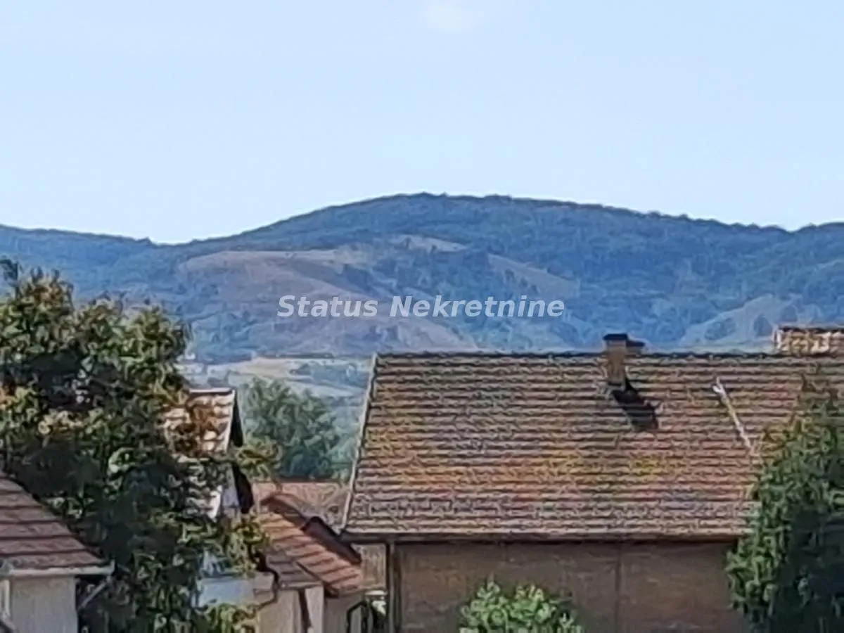 Pogled sa prozora na okolna brda i krovove kuća.