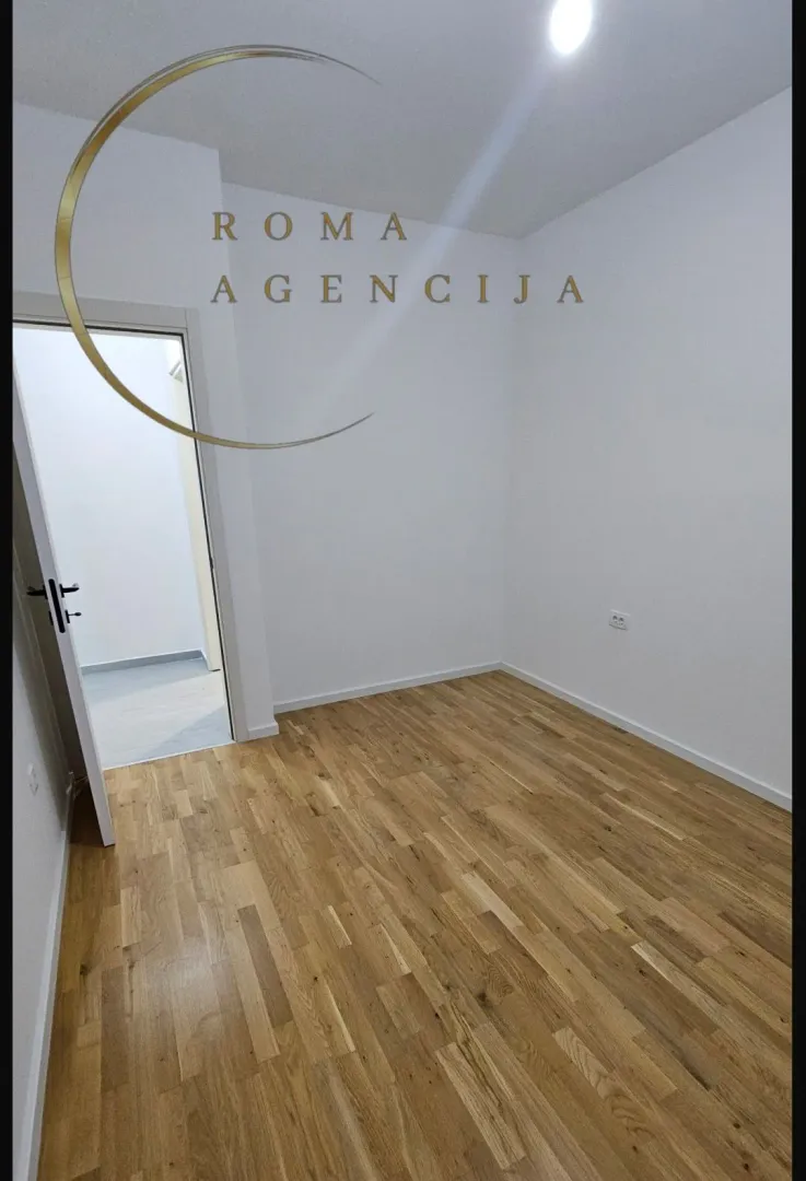 Prazna soba sa drvenim podom i bijelim zidovima.