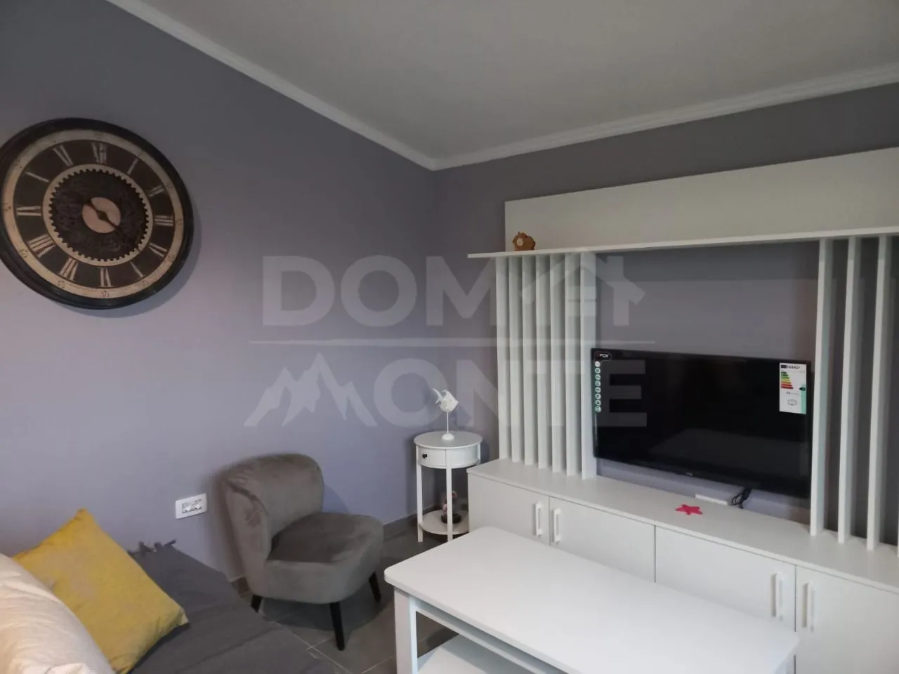 Living room with sofa, TV unit and a large wall clock.