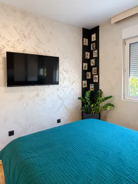 Spavaća soba sa bračnim krevetom, televizorom i ukrasnim detaljima na zidu. - image 6