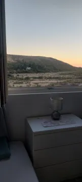 Pogled na brdo kroz prozor iz sobe sa komodom i lampom. - image 9