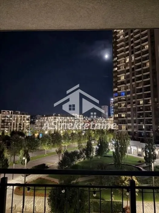 Noćni pogled sa terase na osvetljene gradske zgrade i zelenu površinu.