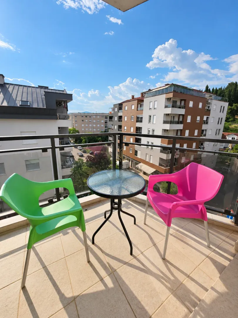 Namtješten balkon sa stolom i dvije stolice u boji i pogledom na grad.
