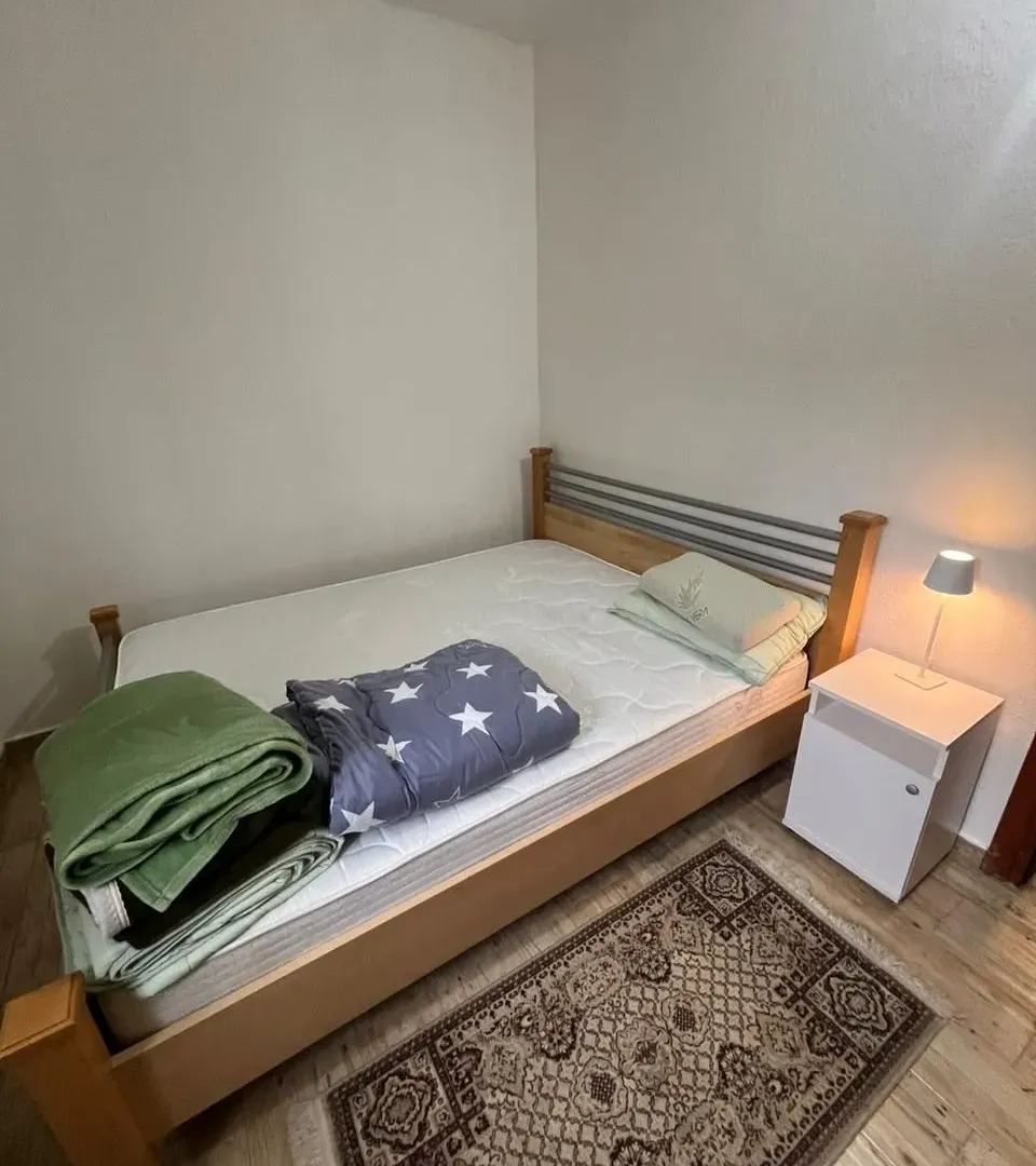 Manja spavaća soba sa bračnim krevetom, noćnim stočićem i tepihom.