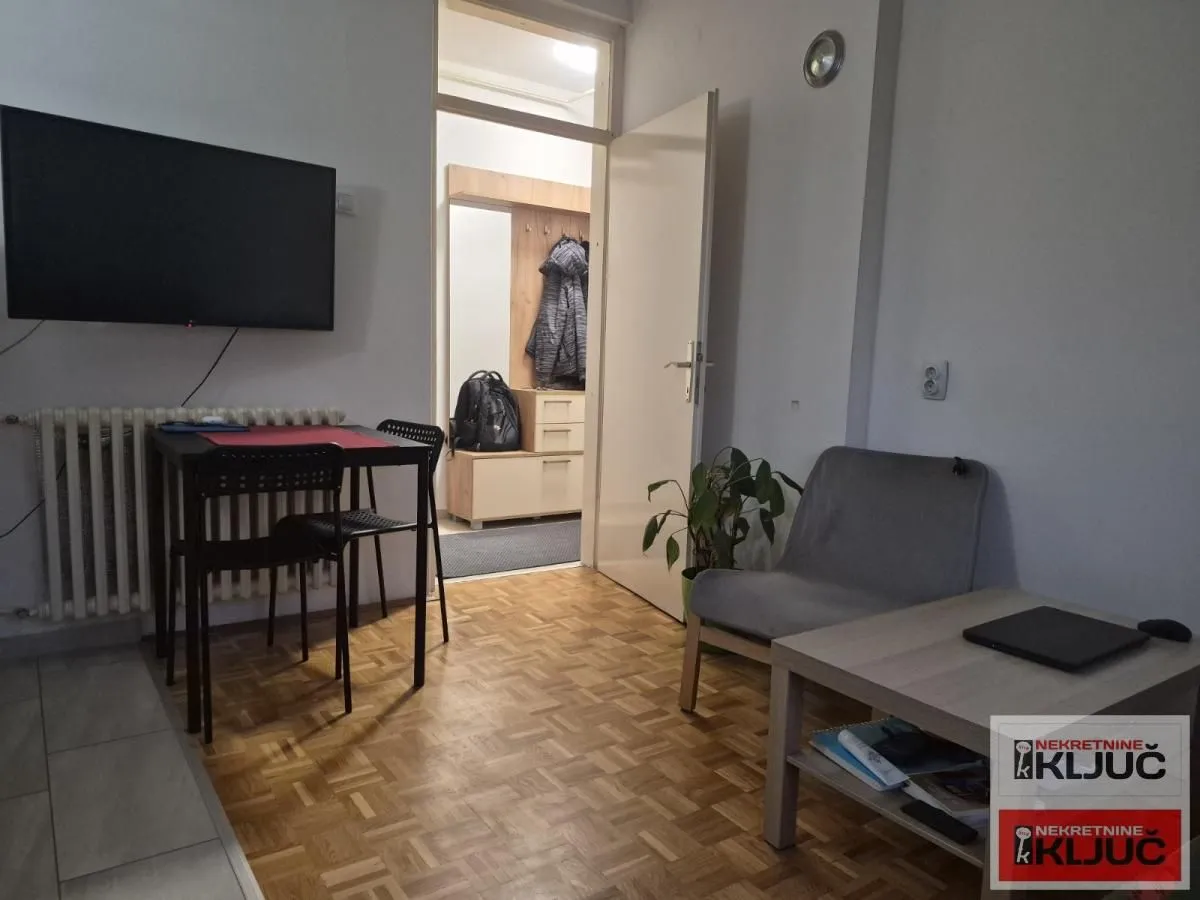 Dnevna soba sa garniturom, televizorom i trpezarijskim stolom.