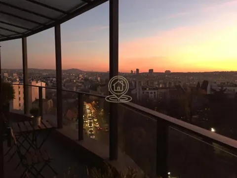 Covered balcony with seating furniture and a city view at dusk. - image 10