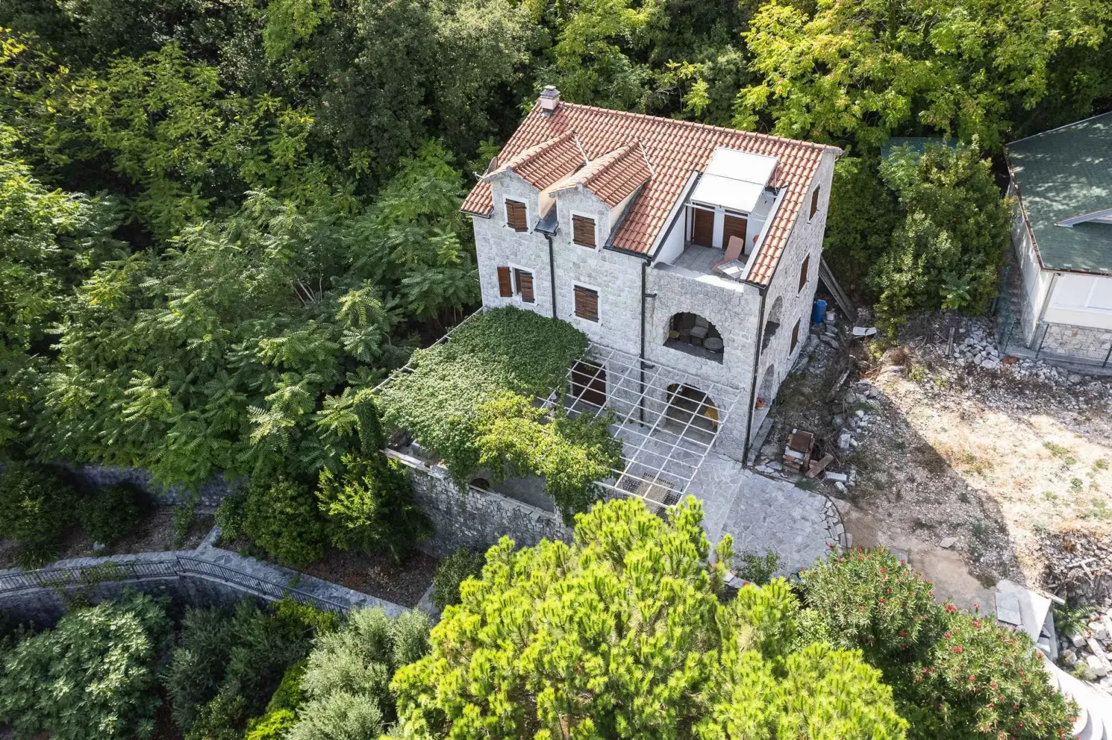 Pogled odozgo na kamenu kuću sa terasom i okolnim zelenilom.